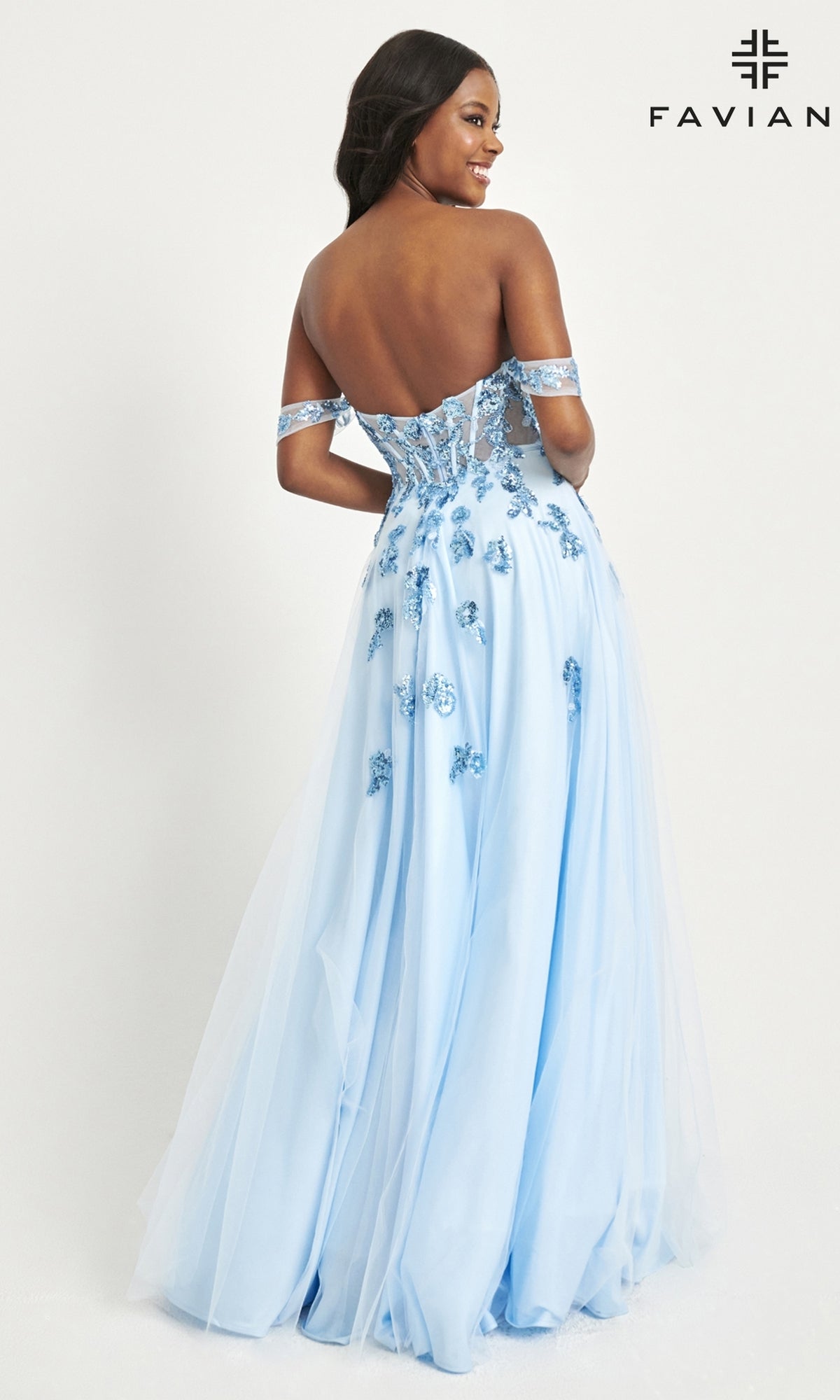 A woman poses with her back to the camera in the Faviana Off-Shoulder Long A-Line Prom Dress 11059—featuring a light blue hue, floral embellishments, a sheer-corset bodice, and an elegant tulle skirt with delicate sheer details.